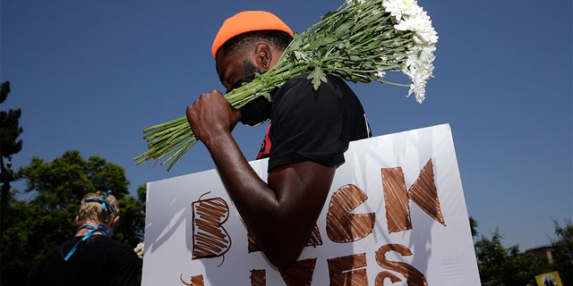 FILE - In this July 20, 2020, file photo, holding flowers and a sign, Blair Toles, 30, attends rally in Los Angeles, on Black Strike Day. Ahead of Labor Day, major U.S. labor unions say they are considering work stoppages in support of the Black Lives Matter movement. (AP Photo/Jae C. Hong, File)