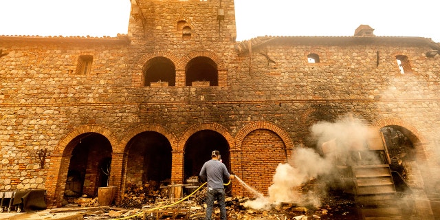 Cellar worker Jose Juan Perez sprays water on burning debris at Castello di Amorosa, Monday, Sept. 28, 2020, in Calistoga, Calif., which was damaged in the Glass Fire.