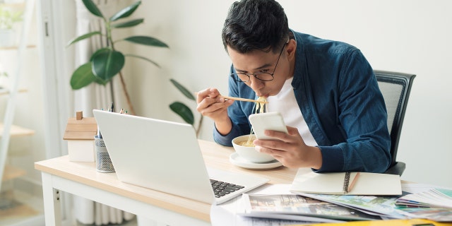 Cheerful man sitting in front of his computer monitor eating and working.