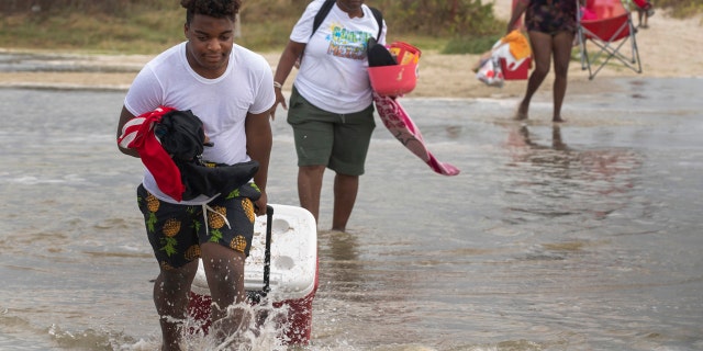 Tyler Heads totes his belongings through tidewaters as he and other beachgoers cross the flooding Stewart Beach parking lot in Galveston, Texas on Saturday, Sept. 19, 2020.