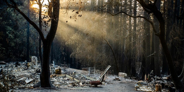Sun rays are highlighted by smoke from the CZU Lighting Complex Fire as remains of a house sit on a parcel off Vick Drive near Empire Grade in Bonny Doon, Calif., on Thursday, Aug., 27, 2020.