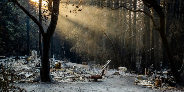 Sun rays are highlighted by smoke from the CZU Lighting Complex Fire as remains of a house sit on a parcel off Vick Drive near Empire Grade in Bonny Doon, Calif., on Thursday, Aug., 27, 2020.