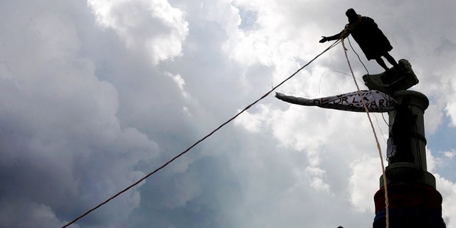 Venezuelan demonstrators use ropes to topple a Christopher Columbus statue in Caracas, October 12, 2004. REUTERS/Jorge Silva