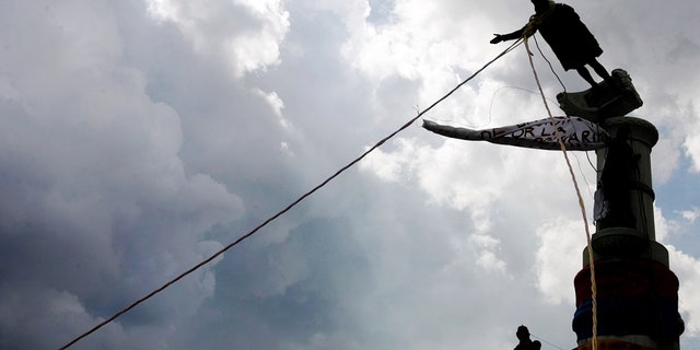 Venezuelan demonstrators use ropes to topple a Christopher Columbus statue in Caracas, October 12, 2004. REUTERS/Jorge Silva