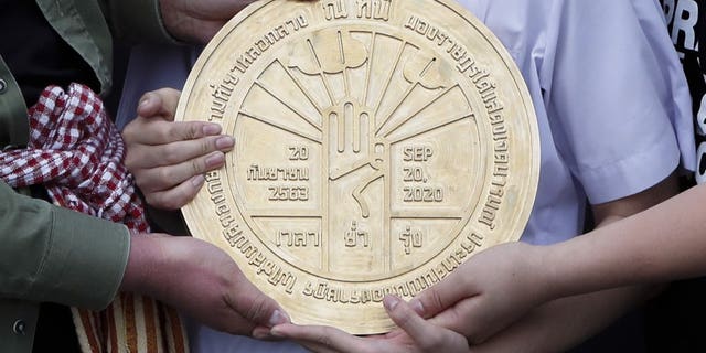 Pro-democracy student leaders hold a plaque declaring "This country belongs to the people" at the Sanam Luang field during a protest in Bangkok, Thailand, Sunday, Sept. 20, 2020. Thousands of demonstrators turned out Saturday for a rally to support the student-led protest movement's demands for new elections and reform of the monarchy. (AP Photo/Sakchai Lalit)
