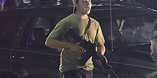 Aug. 25, 2020: Kyle Rittenhouse carries a weapon as he walks along Sheridan Road in Kenosha, Wis., during a night of unrest following the weekend police shooting of Jacob Blake. The way his lawyers tell it, the teenager wasn't a scared, gun enthusiast in over his head when he fatally shot two protesters. He was a courageous defender of liberty, a patriot exercising his right to bear arms amid chaos in the streets. But some legal experts say Rittenhouse's lawyers are taking big risks by turning a fairly straightforward self-defense case into a sweeping political argument that mirrors the law-and-order re-election campaign of President Donald Trump. (Adam Rogan/The Journal Times via AP)
