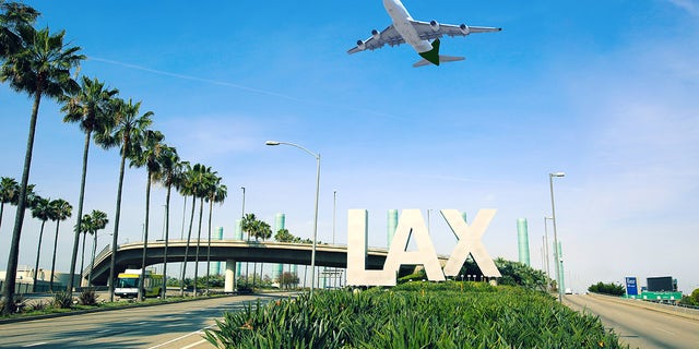 A Los Angeles Airport (LAX) sign is seen with a jet flying overhead.