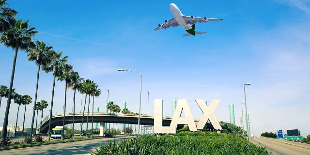 Los Angeles Airport sign full highway with airplane flying overhead.