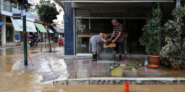 Residents clean a sheet of glass next to a flooded street after a storm at Karditsa town, Saturday, Sept. 19, 2020.