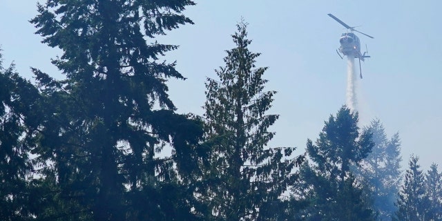 A helicopter makes a water drop, Wednesday, Sept. 9, 2020, on a hotspot of a wildfire burning in Bonney Lake, Wash., south of Seattle.