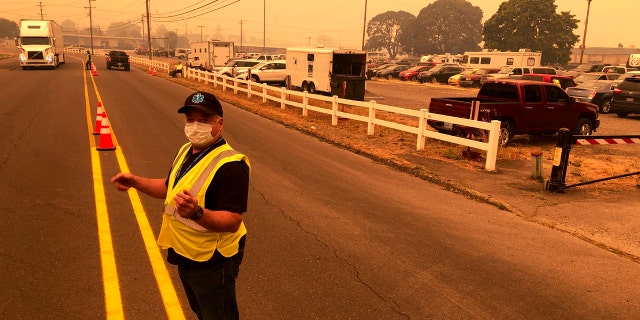 Under a smoke-filled sky, volunteer Shawn Daley directs traffic into the parking lot an evacuation center at the Oregon State Fairgrounds, which was crowded with hundreds of cars, pickup trucks, and campers of evacuees, in Salem on Tuesday, Sept. 8, 2020.