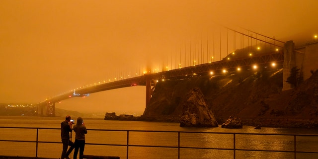 Patrick Kenefick, left, and Dana Williams, both of Mill Valley, Calif., record the darkened Golden Gate Bridge covered with smoke from wildfires Wednesday, Sept. 9, 2020, from a pier at Fort Baker near Sausalito, Calif. The photo was taken at 9:47 a.m. in the morning.