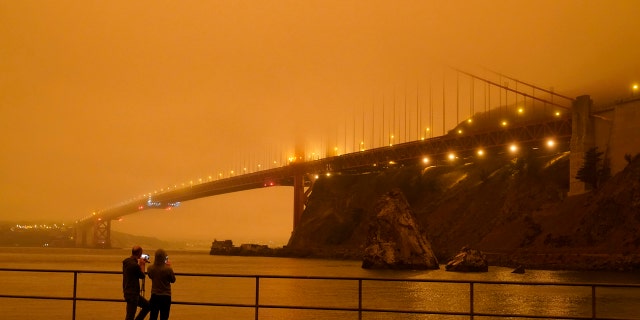 Patrick Kenefick, left, and Dana Williams, both of Mill Valley, Calif., record the darkened Golden Gate Bridge covered with smoke from wildfires Wednesday, Sept. 9, 2020, from a pier at Fort Baker near Sausalito, Calif. The photo was taken at 9:47 a.m. in the morning.