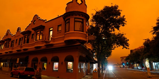 A woman crosses a street by in front of a hotel as smoke from wildfires darken the morning sky Wednesday, Sept. 9, 2020, in Sausalito, California.