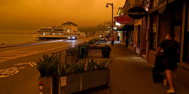 A man walks along Bridgeway Avenue and looks out at the darkened morning sky with smoke from wildfires Wednesday, Sept. 9, 2020, in Sausalito, Calif.
