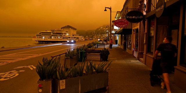 A man walks along Bridgeway Avenue and looks out at the darkened morning sky with smoke from wildfires Wednesday, Sept. 9, 2020, in Sausalito, Calif.