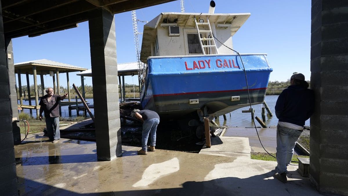 Boat owner Ricky Mitchell, center, and his friend Buck, left, no last name given, survey damage to his boat that washed up against the home of Ray Garcia, in Lakeshore, Miss., Thursday, Oct. 29, 2020. Hurricane Zeta passed through Wednesday with a tidal surge that caused the boat to become unmoored. (AP Photo/Gerald Herbert)