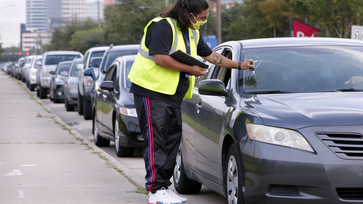 Volunteer Sharely Gomez marks the windshield after taking information from clients in their cars as they wait for food distribution at West Houston Assistance Ministries on Wednesday, Oct. 14, 2020, in Houston. (AP Photo/Michael Wyke)