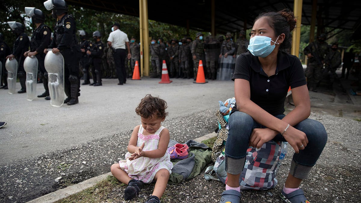 An Honduran migrant and her daughter sit at a roadblock set by security forces in Poptun, Guatemala, Friday, Oct. 2, 2020. Guatemala vowed to detain and return members of a new caravan of hundreds of migrants that set out from neighboring Honduras in hopes of reaching the United States, saying they represent a health threat amid the coronavirus pandemic. (AP Photo/Moises Castillo)