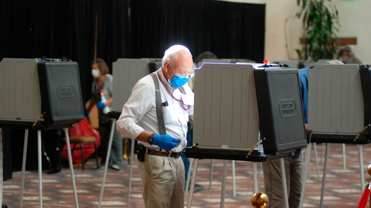Temporary election worker Joseph Banar disinfects voting stations as a precaution against the coronavirus, while a steady stream of voters participates in the first day of balloting in New Mexico at the Santa Fe Convention Center on Tuesday, Oct. 6, 2020. (AP Photo/Morgan Lee)