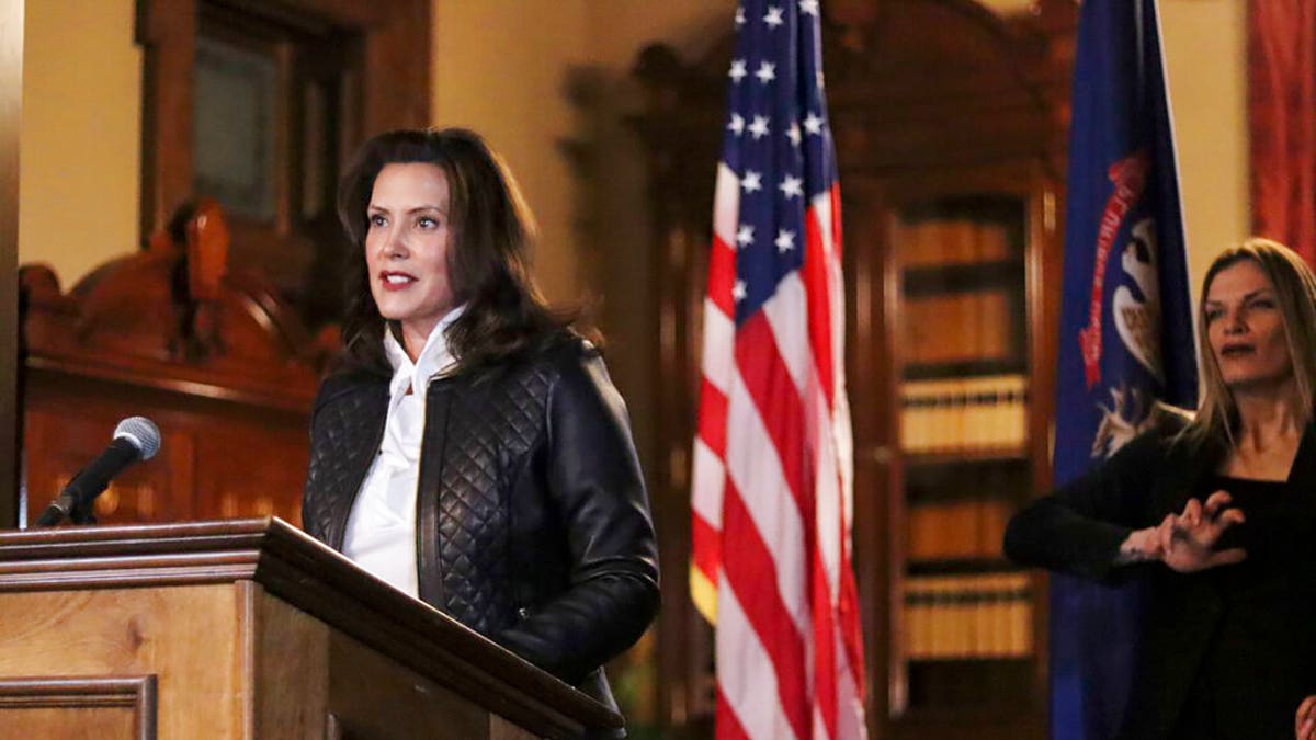 Governor Gretchen Whitmer in a black coat in front of U.S. and Michigan flags