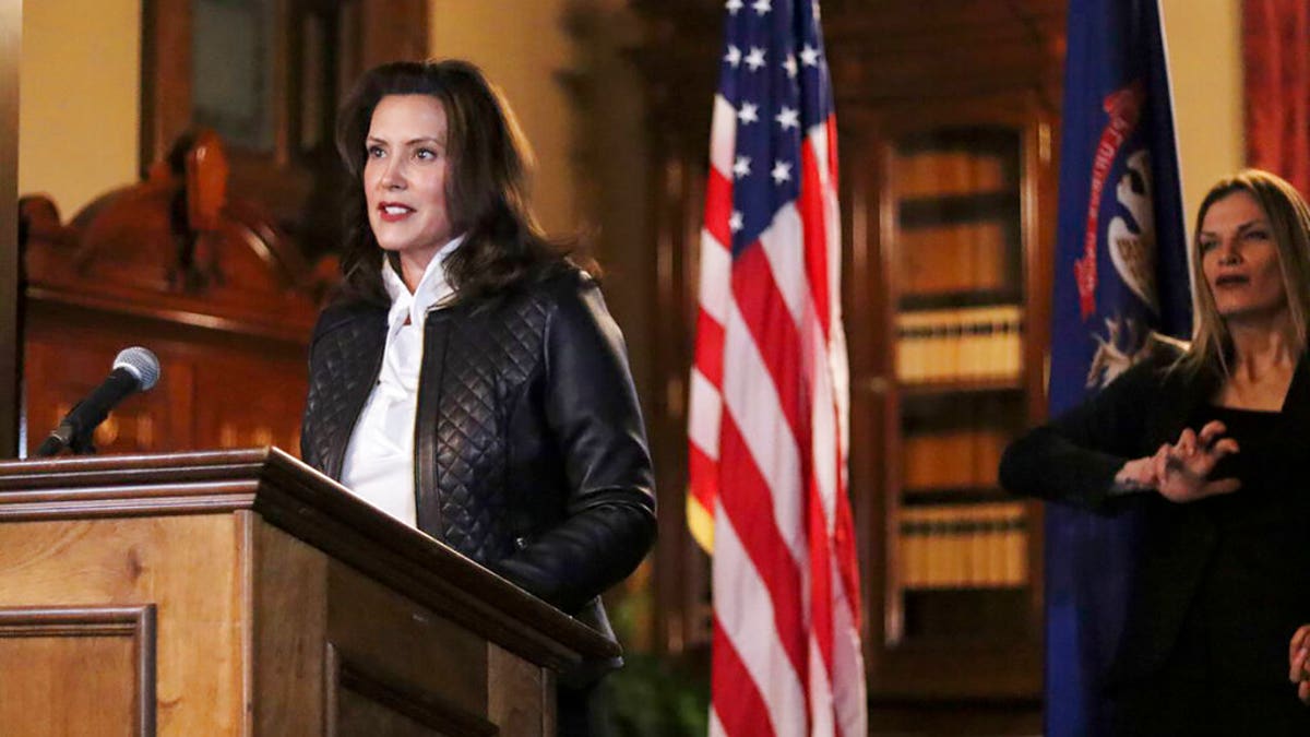 Governor Gretchen Whitmer in a black coat in front of U.S. and Michigan flags