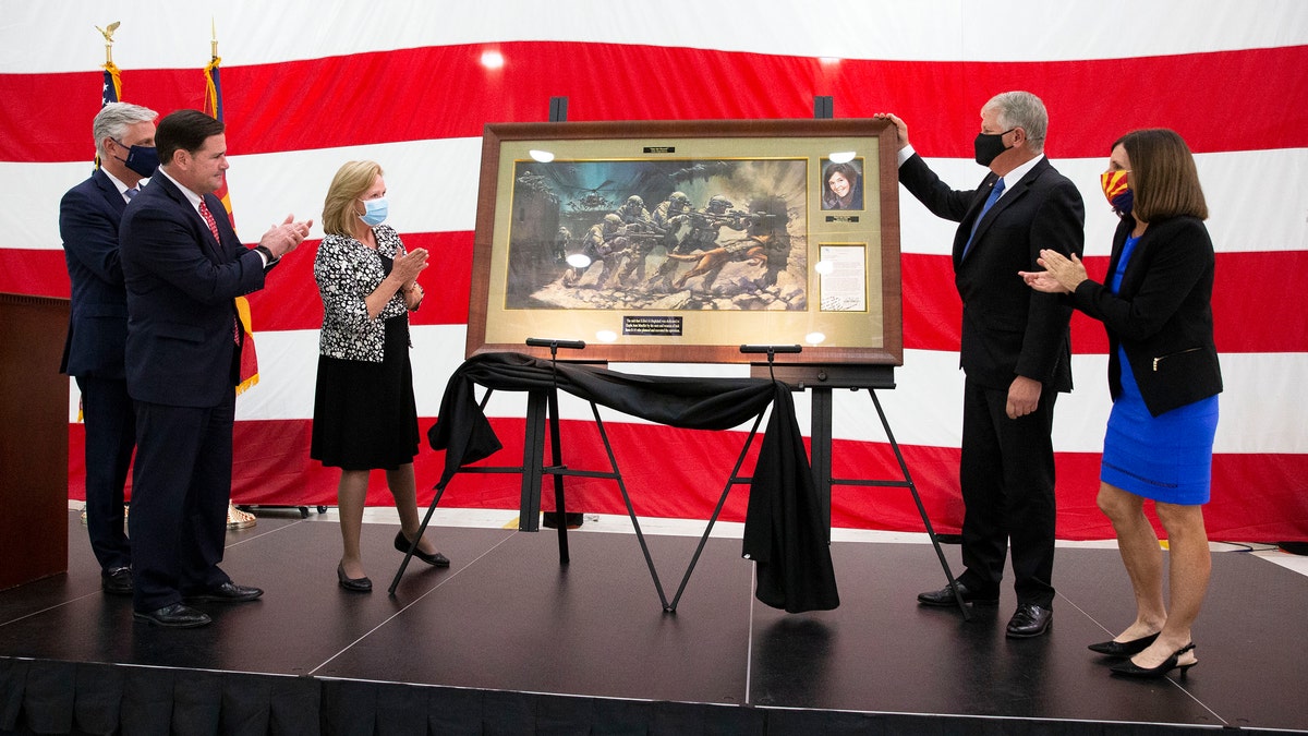 From left, U.S. national security adviser Robert O'Brien, Arizona Gov. Doug Ducey, parents Marsha and Carl Mueller, and U.S. Sen. Martha McSally, R-Ariz, applaud during a ceremony to unveil a painting honoring Kayla Mueller, a humanitarian and Prescott native, at the Goldwater Air National Guard Base, Thursday, Oct. 8, 2020, in Phoenix.  (Rob Schumacher/The Arizona Republic via AP)