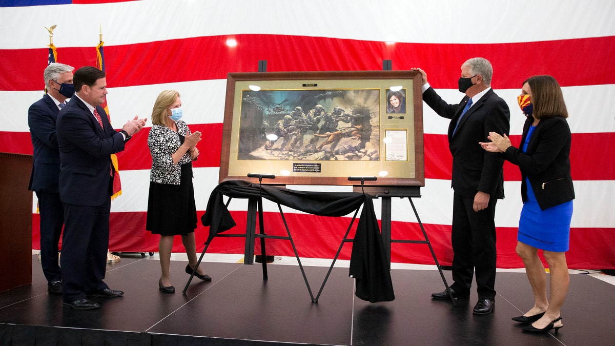 From left, U.S. national security adviser Robert O'Brien, Arizona Gov. Doug Ducey, parents Marsha and Carl Mueller, and U.S. Sen. Martha McSally, R-Ariz, applaud during a ceremony to unveil a painting honoring Kayla Mueller, a humanitarian and Prescott native, at the Goldwater Air National Guard Base, Thursday, Oct. 8, 2020, in Phoenix. (Rob Schumacher/The Arizona Republic via AP)