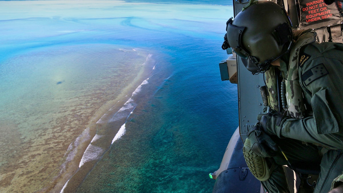 In this Sept. 25, 2020, photo provided by the Royal Australian Navy, Leading Seaman Daniel Atkins looks out over Elizabeth Reef in search of unexploded ordnance on an MRH-90 helicopter from HMAS Adelaide. The 45-kilogram (100-pound) bomb was found by a fisherman on Elizabeth Reef near Lord Howe Island, about 550 kilometers (340 miles) off New South Wales state. (Sgt. Jake Sims/Royal Australian Navy via AP)