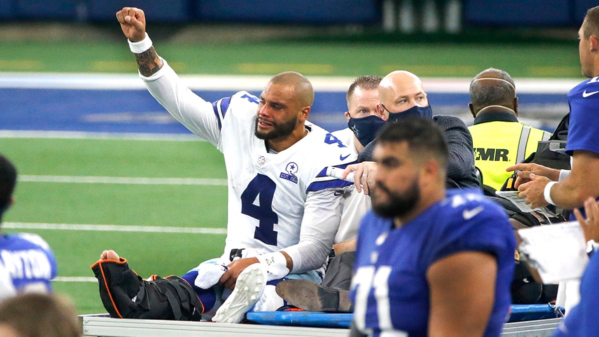 Dallas Cowboys quarterback Dak Prescott (4) lifts his fist to cheers from fans as he is carted off the field after suffering a lower right leg injury running the ball in the second half of an NFL football game against the New York Giants in Arlington, Texas, Sunday, Oct. 11, 2020. (AP Photo/Michael Ainsworth)