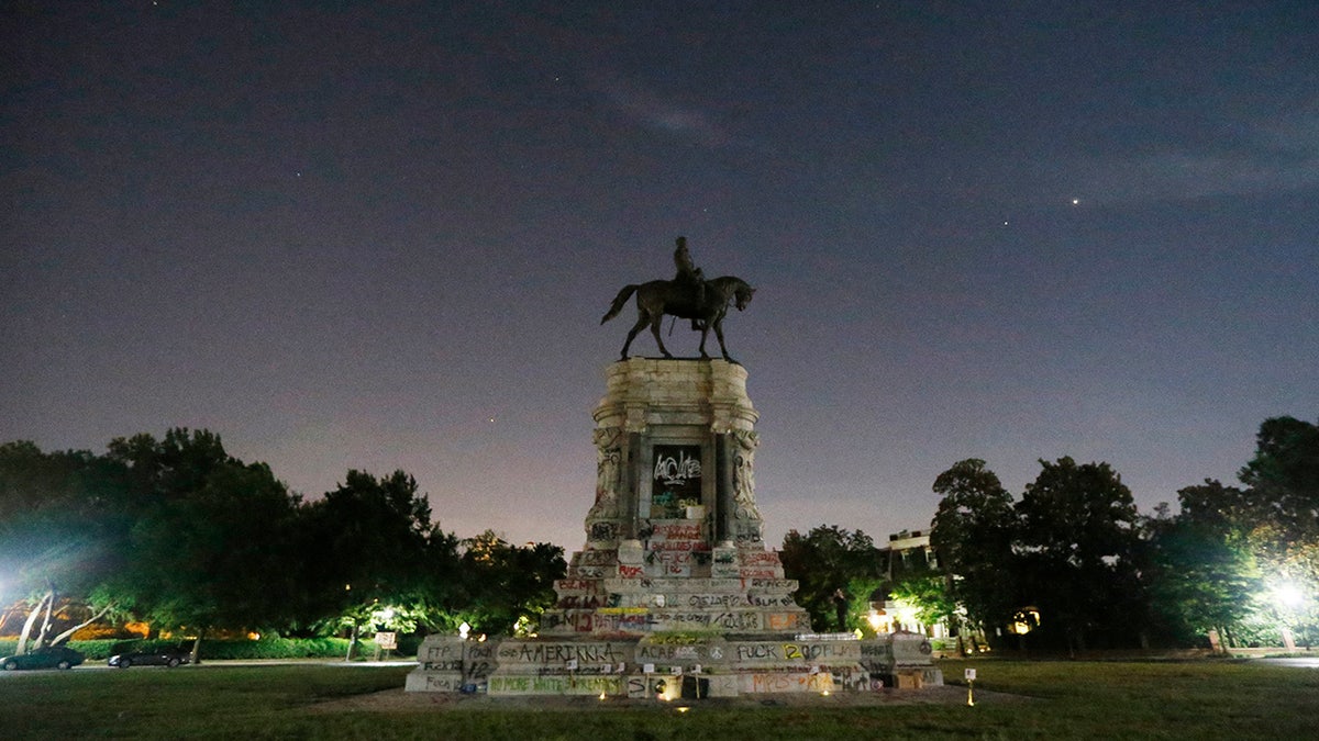 The moon and street lights illuminate the statue of Confederate General Robert E. Lee on Monument Avenue Friday June. 5, 2020, in Richmond, Va. A lawsuit seeking to prevent Virginia Gov. Ralph Northam from removing the statue is scheduled to go to trial Monday, Oct. 19, 2020. (AP Photo/Steve Helber)