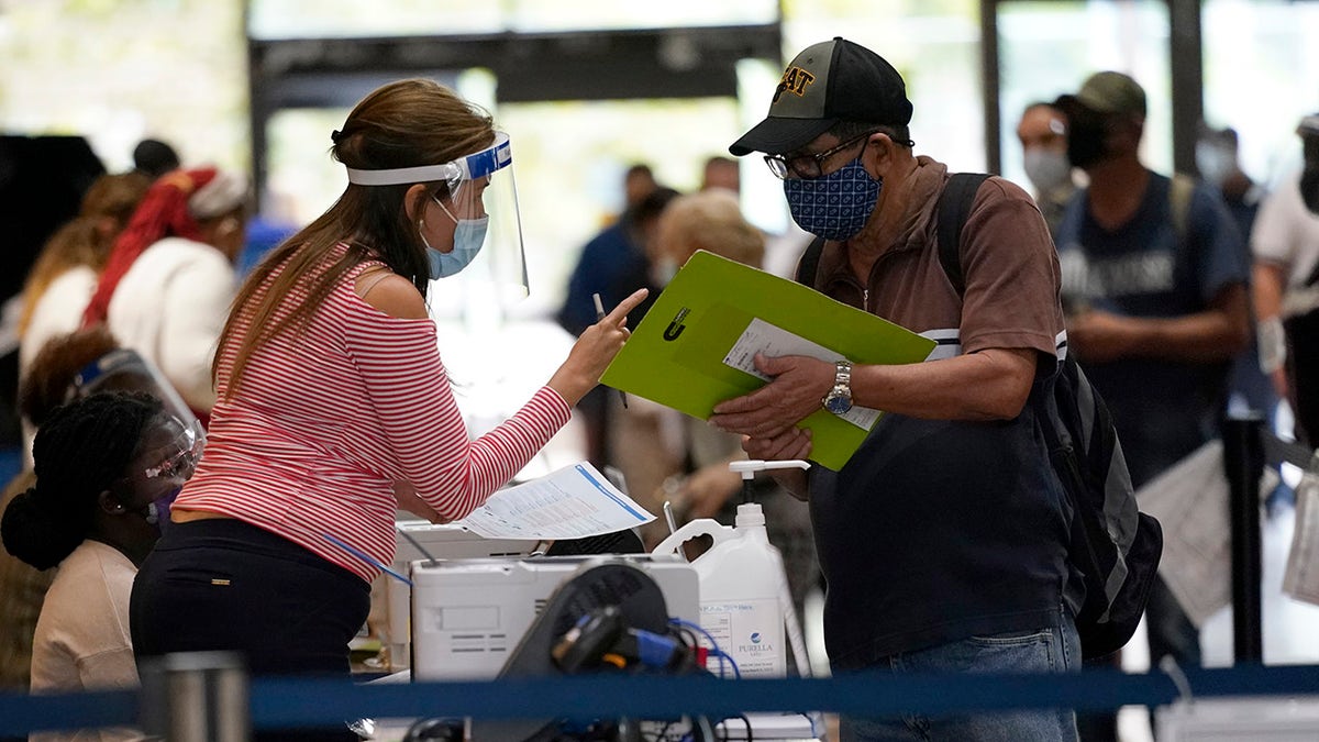 An election worker, left, gives instructions for voting at an early voting site, Monday, Oct. 19, 2020, in Miami. Florida begins in-person early voting in much of the state Monday. With its 29 electoral votes, Florida is crucial to both candidates in order to win the White House. (AP Photo/Lynne Sladky)