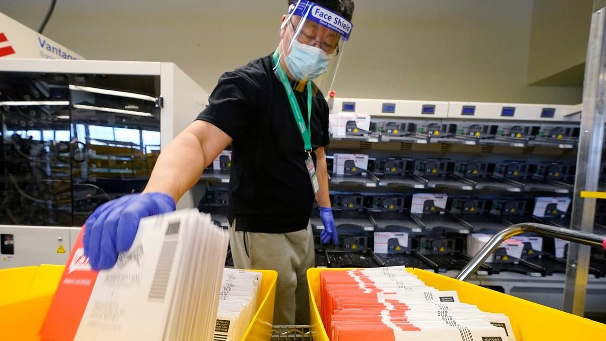 An election worker moves returned ballots from a sorting machine behind at the King County Elections office Tuesday, Oct. 20, 2020, in Renton, Wash. (AP Photo/Elaine Thompson)
