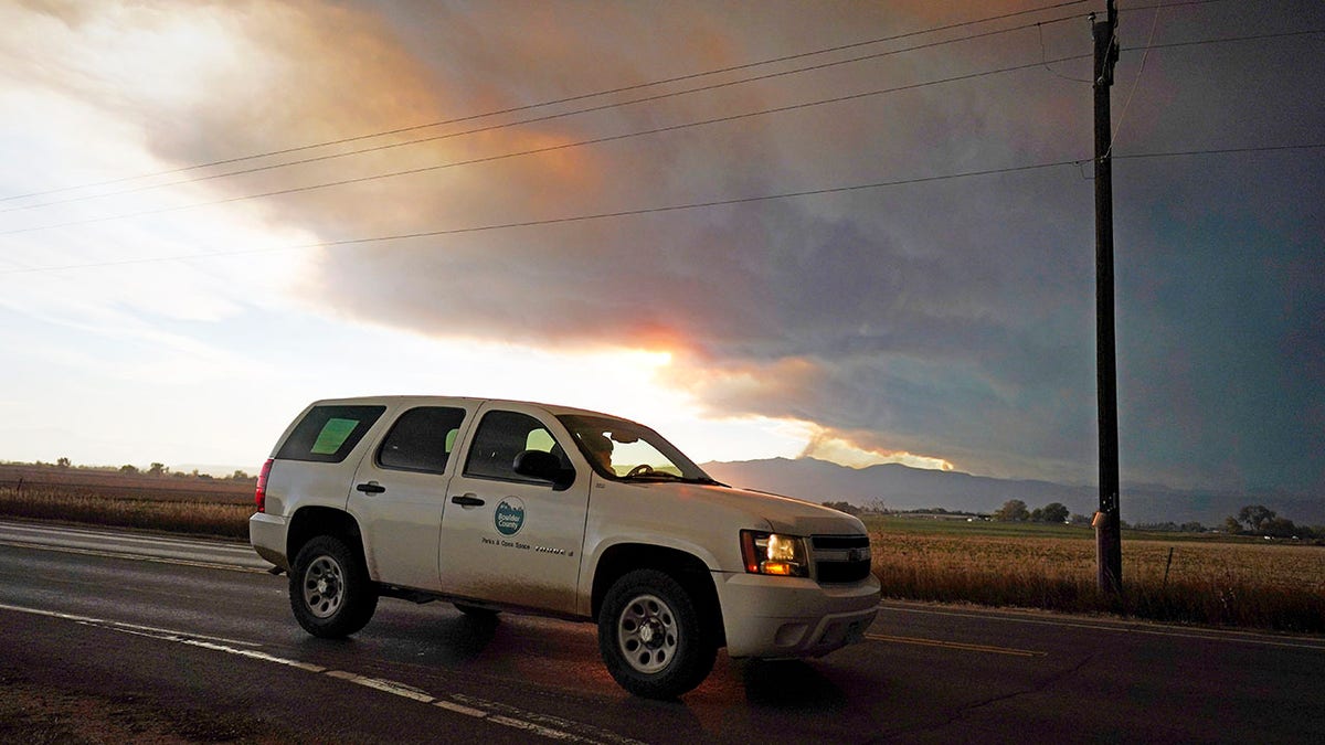 Smoke rises from mountain ridges as several wildfires burn in the state Wednesday, Oct. 21, 2020, as traffic moves along 75th street in Niwot, Colo. (Associated Press)