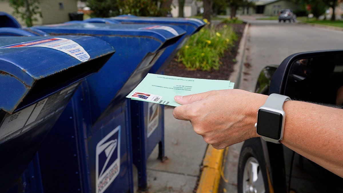 A person drops applications for mail-in-ballots into a mailbox in Omaha, Neb. (AP Photo/Nati Harnik, File)