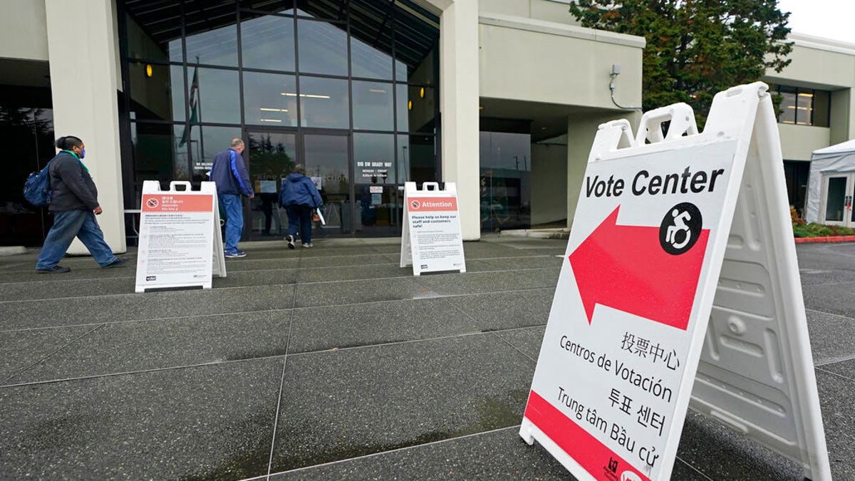 People walk near a sign at the King County election headquarters Oct. 23, 2020.