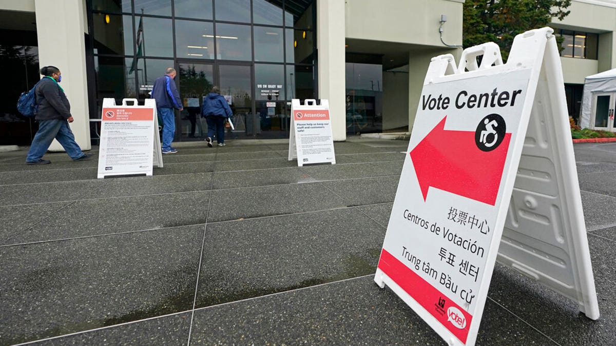 People walk near a sign at the King County election headquarters Oct. 23, 2020.