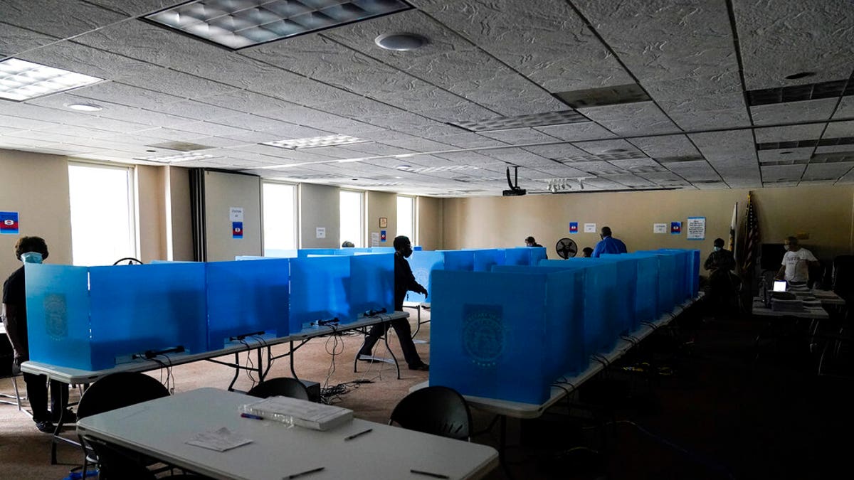Poll workers walk through dark voting booths during early voting at the Dunwoody Library after Hurricane Zeta knocked out power in the surrounding areas on Oct. 29, in Dunwoody, Ga.