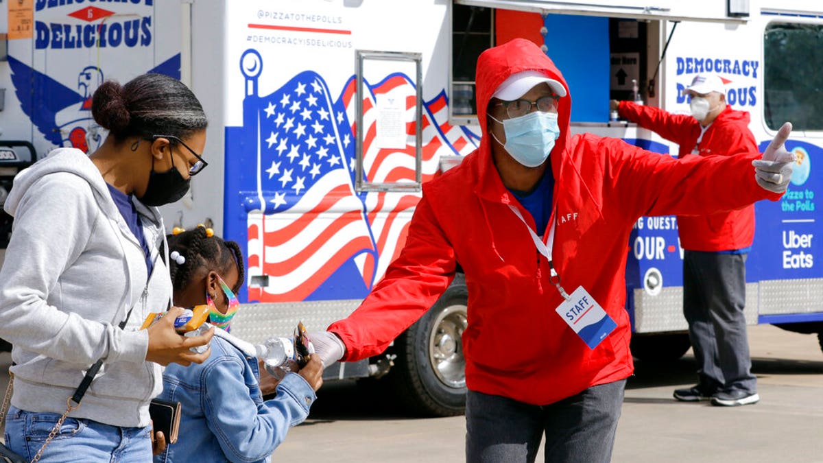 A staff member distributes water and snacks in front of the Democracy is Delicious food truck, powered by Pizza to the Polls and Uber Eats, Thursday, Oct. 29, 2020 in Houston. 