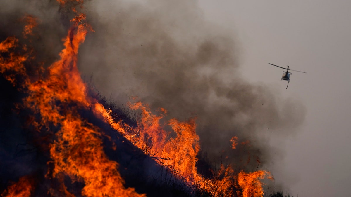 A helicopter flies away after dropping water over the Blue Ridge Fire burning along the 71 state highway Tuesday, Oct. 27, 2020, in Chino Hills, Calif.