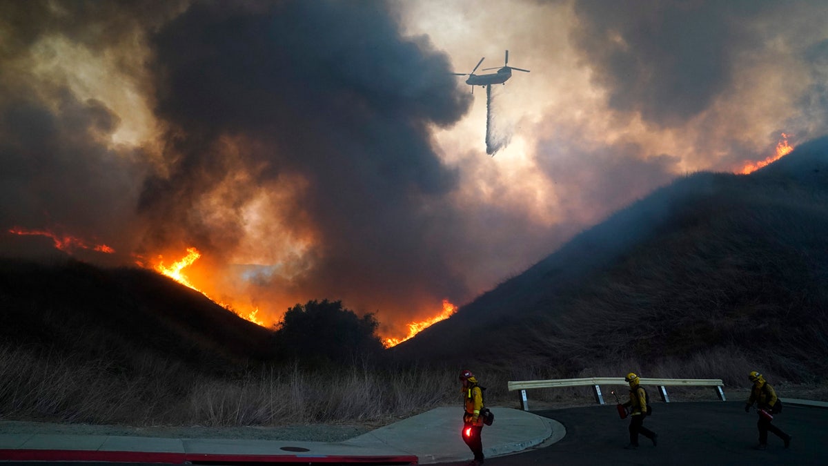 A helicopter drops water as firefighters walk with drip torches to set a backfire against the Blue Ridge Fire on Tuesday, Oct. 27, 2020, in Chino Hills, Calif.