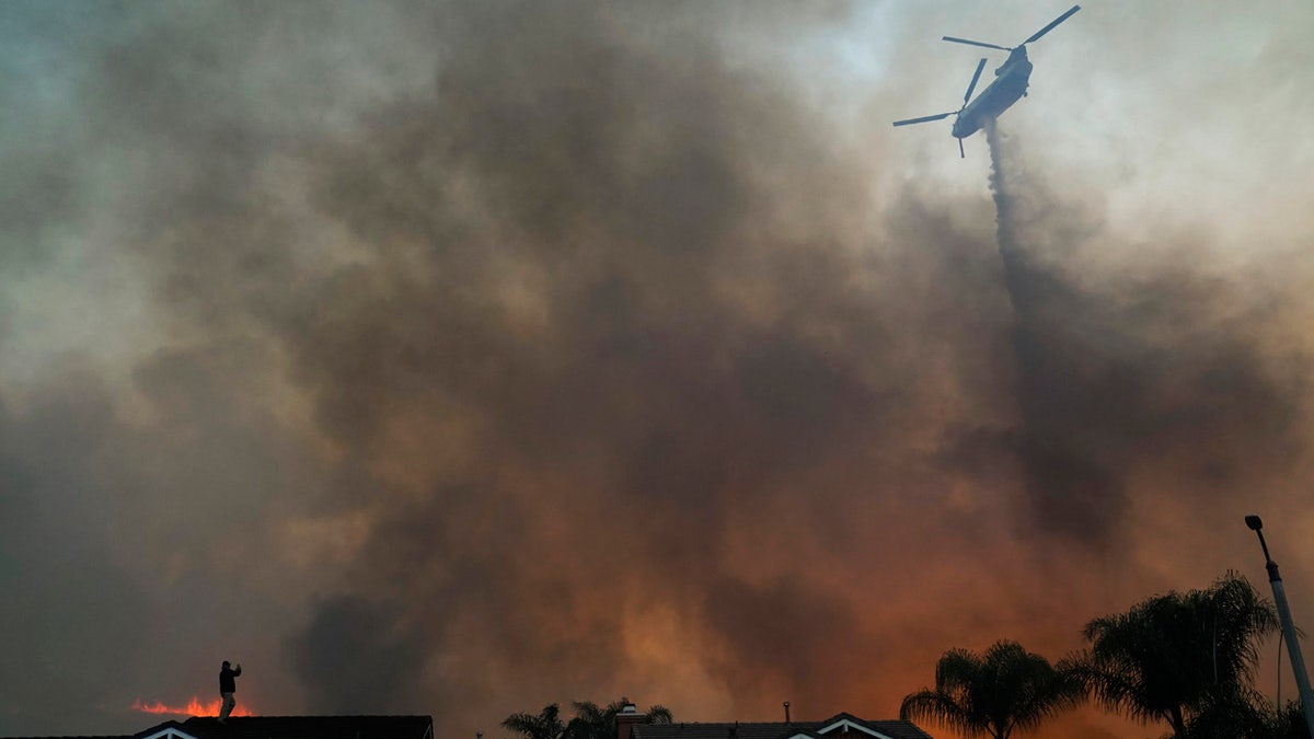 Herman Termeer, bottom left, takes pictures as a helicopter drops water over the Blue Ridge Fire burning along the hillside Tuesday, Oct. 27, 2020, in Chino Hills, Calif.