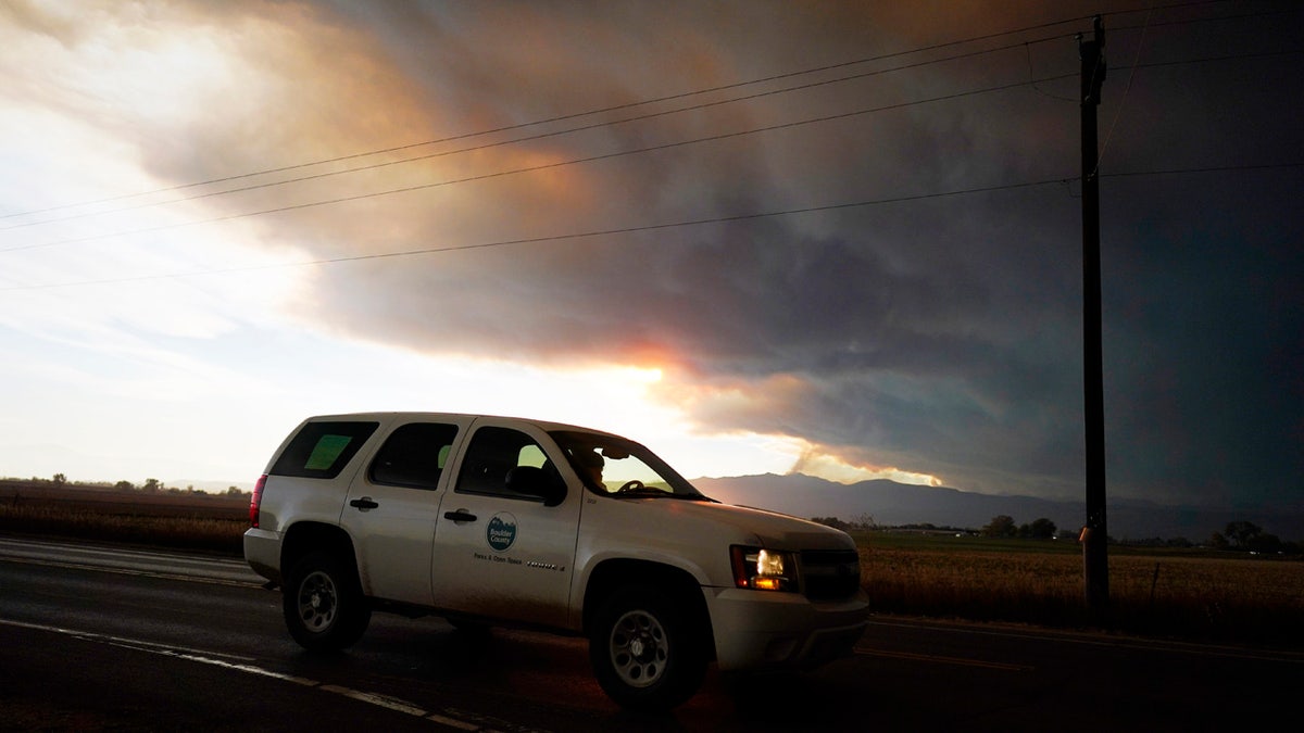Smoke rises from mountain ridges as several wildfires burn in the state Wednesday, Oct. 21, 2020, as traffic moves along 75th street in Niwot, Colo.