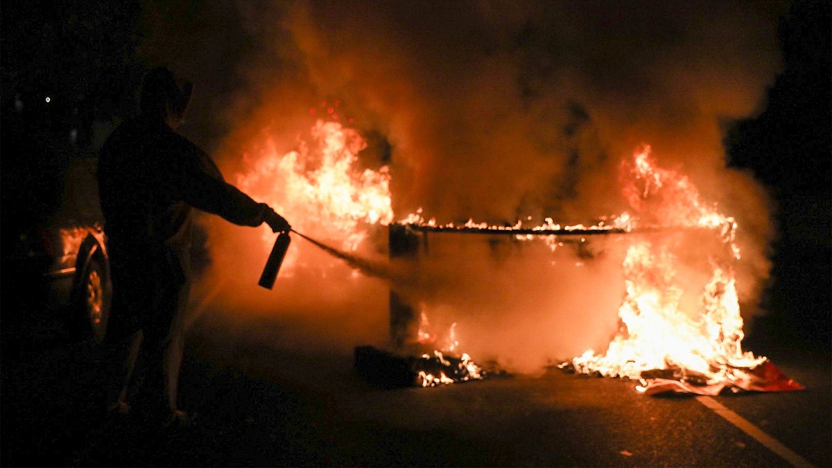 A person uses a fire extinguisher to put out a burning barricade in Philadelphia on October 27, 2020, during a protest over the police shooting of 27-year-old Black man Walter Wallace. - Hundreds of people demonstrated in Philadelphia late on October 27, with looting and violence breaking out in a second night of unrest after the latest police shooting of a Black man in the US.  (Photo by Gabriella AUDI / AFP) (Photo by GABRIELLA AUDI/AFP via Getty Images)