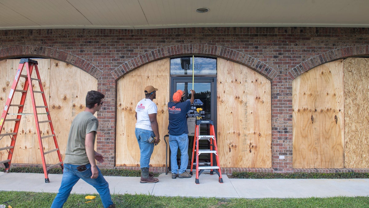 Bernie Arnould, center, gets help from Kaden Ashley and D.J. Hebert, left, all with Pelican Companies, as they board up the windows to the front of MC Bank in Amelia, La., Wednesday, Oct., 7, 2020, in In preparation for Hurricane Delta.