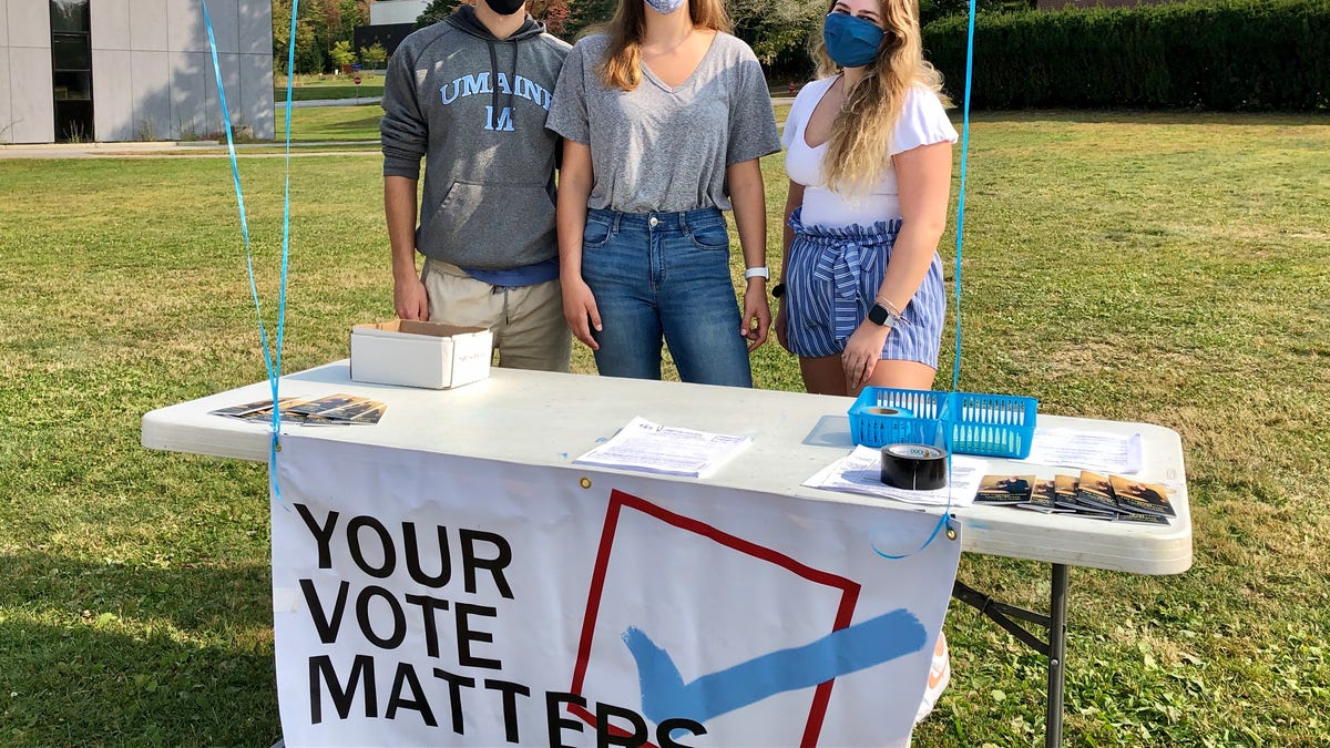 Three students on the campus of the University of Maine work a voter registration table amid the pandemic.