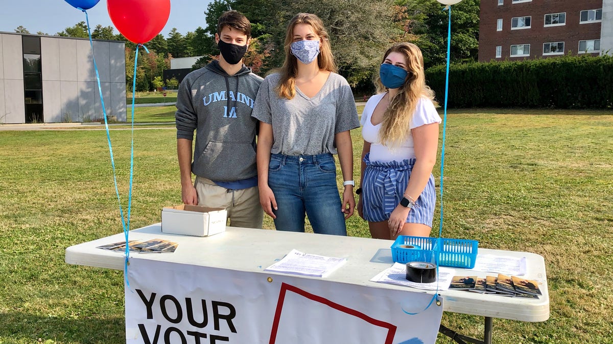 Three students on the campus of the University of Maine work a voter registration table amid the pandemic.