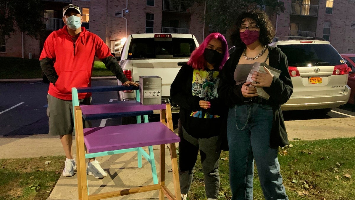 In this photo provided by Jessica Berrellez, her husband, Al Berrellez, left, and daughter Bella Berrellez, right, drop off free desks for Karla Mendez on Tuesday, Sept. 15, 2020, in Gaithersburg, Md.