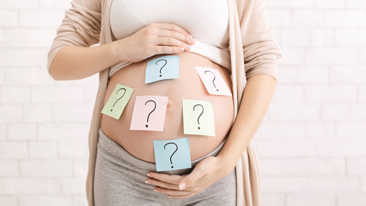 Woman holds pregnant belly with question mark sticky notes