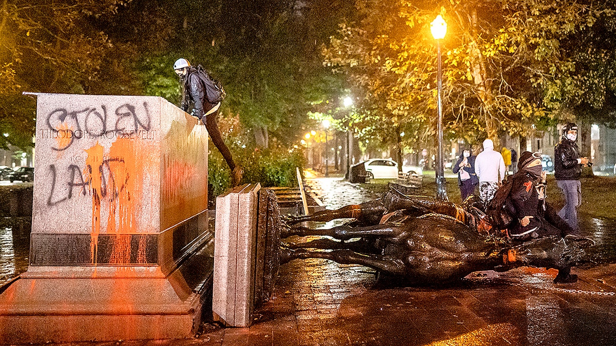 Protesters stand over a toppled statue of President Theodore Roosevelt during an Indigenous Peoples Day of Rage protest on October 11, 2020 in Portland, Oregon. (Photo by Nathan Howard/Getty Images)